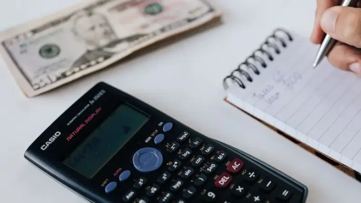 A crop person counting savings using notebook and calculator